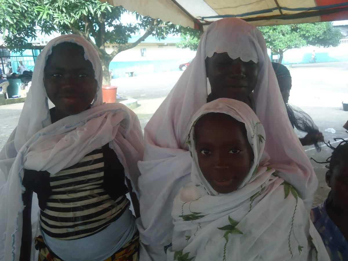 Three smiling girls in white headscarves at a community event