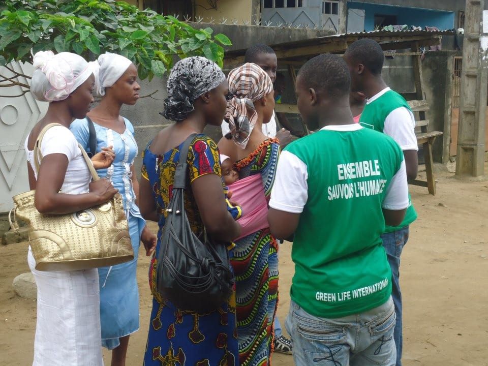 Volunteers in green T-shirts talking with women in the street about a health day